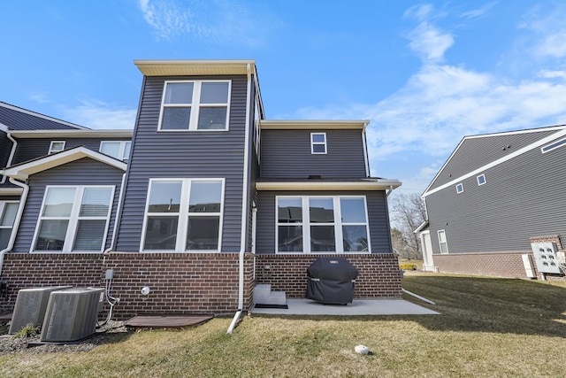 back of house featuring brick siding, a patio area, a lawn, and central AC