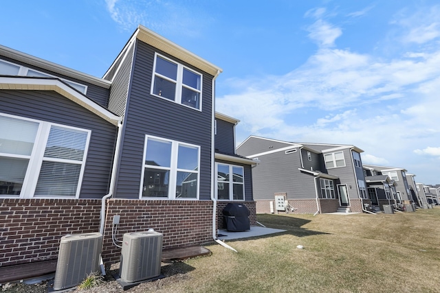 rear view of house featuring central air condition unit, brick siding, and a lawn