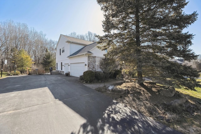 view of side of property featuring stone siding, driveway, an attached garage, and a shingled roof