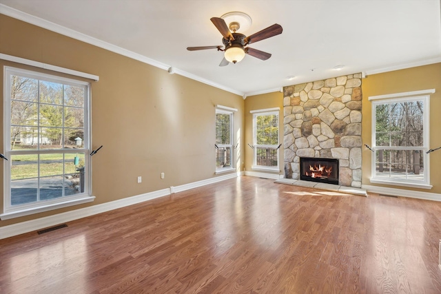 unfurnished living room featuring a stone fireplace, crown molding, wood finished floors, and visible vents