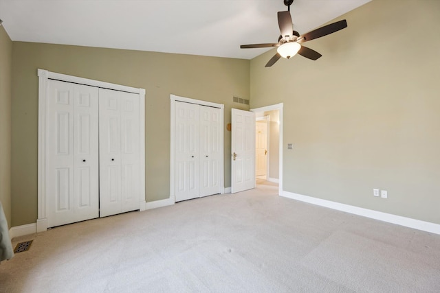 unfurnished bedroom with light colored carpet, two closets, and baseboards