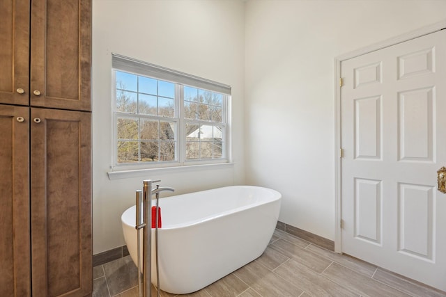 bathroom with a soaking tub, baseboards, and wood finish floors