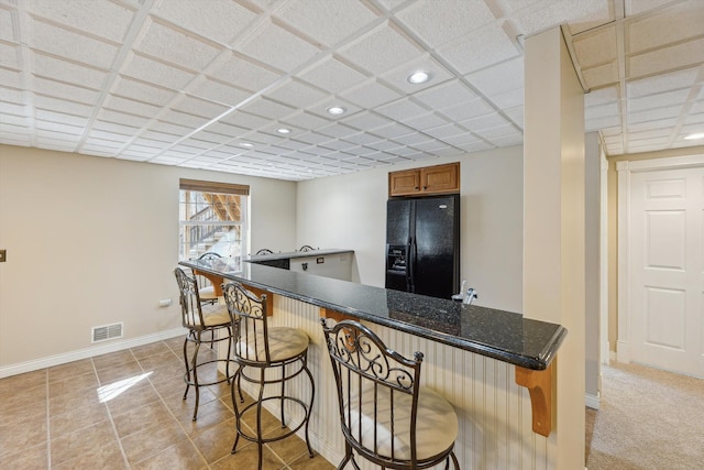 kitchen featuring visible vents, a kitchen breakfast bar, baseboards, and black refrigerator with ice dispenser