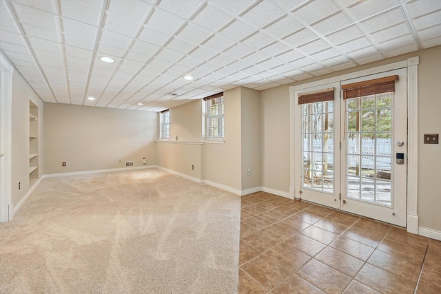 tiled empty room featuring baseboards, built in shelves, carpet floors, and a healthy amount of sunlight