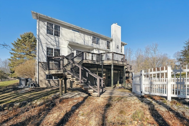 back of house featuring a chimney, stairs, a deck, and fence