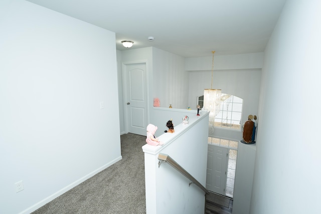 hallway featuring carpet, baseboards, a notable chandelier, and an upstairs landing