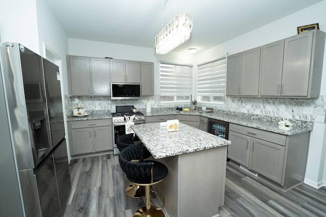 kitchen featuring stainless steel appliances, a kitchen breakfast bar, gray cabinets, decorative backsplash, and a center island