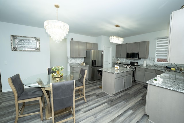 kitchen featuring appliances with stainless steel finishes, a center island, an inviting chandelier, gray cabinets, and a sink