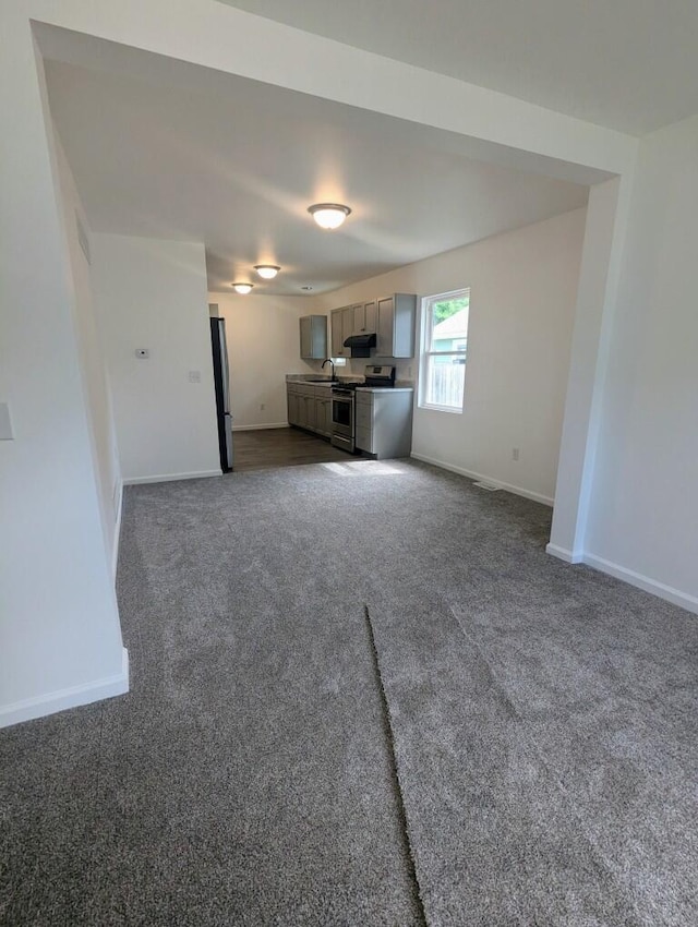 unfurnished living room featuring baseboards, dark carpet, and a sink