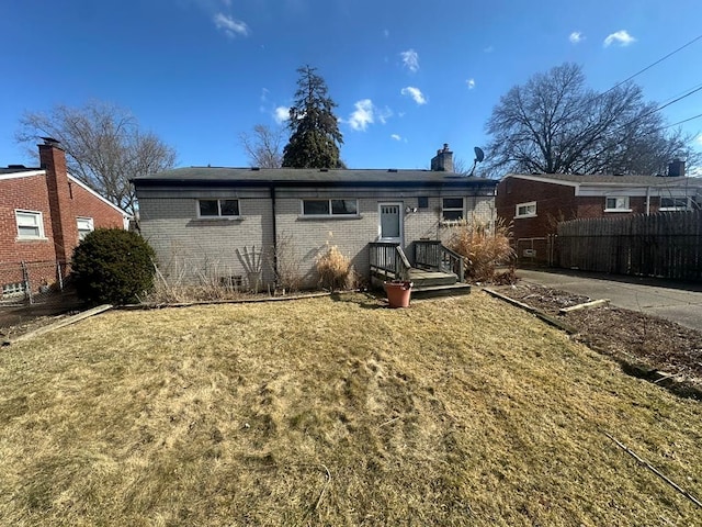 rear view of property featuring a chimney, fence, a lawn, and brick siding