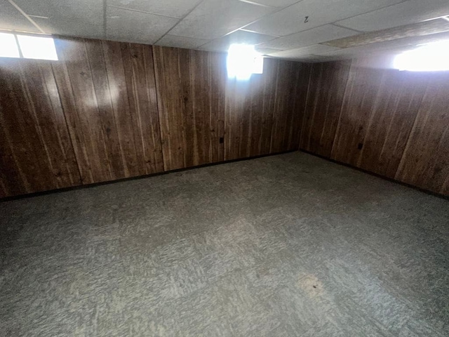 below grade area featuring a paneled ceiling, wood walls, and carpet floors