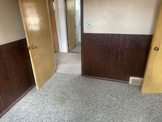 hall with wainscoting, wood walls, visible vents, and carpet flooring