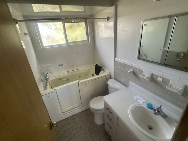 bathroom featuring toilet, tile patterned floors, a whirlpool tub, vanity, and tile walls