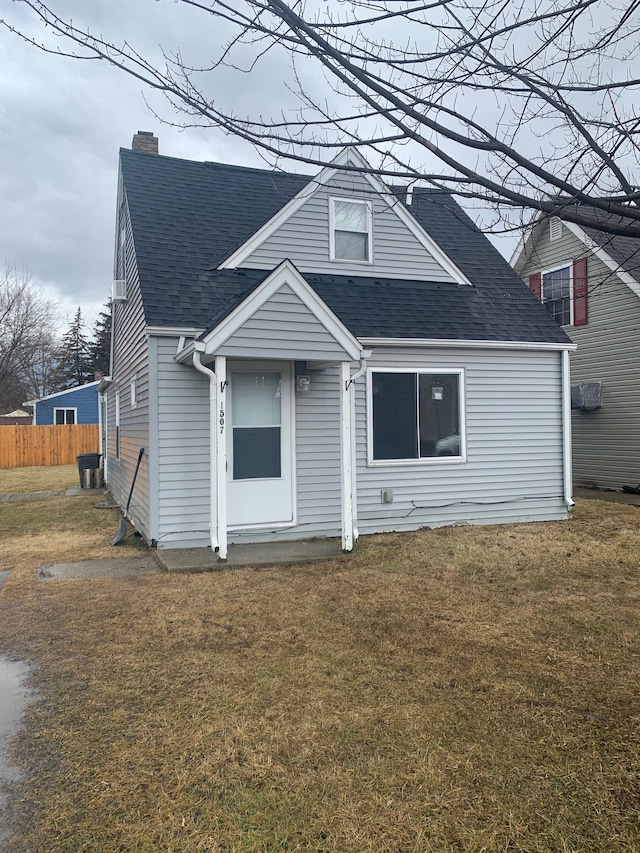 view of front of property featuring a shingled roof, a chimney, a front yard, and fence