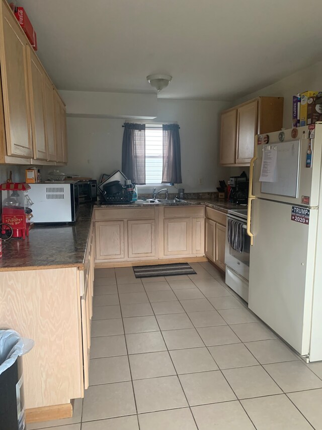 kitchen with light tile patterned floors, a sink, range, freestanding refrigerator, and dark countertops