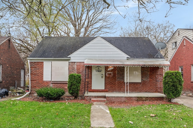 bungalow featuring covered porch, roof with shingles, a front lawn, and brick siding