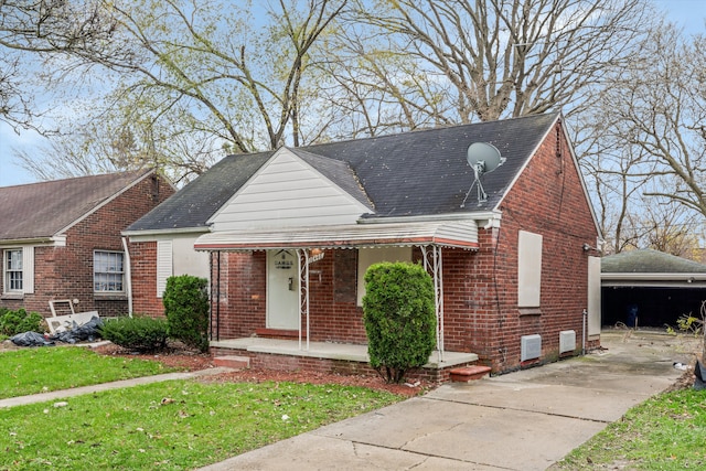 view of front facade with covered porch, brick siding, roof with shingles, and an outbuilding