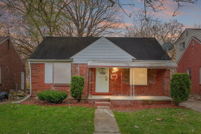 bungalow-style home with a yard, brick siding, and a shingled roof