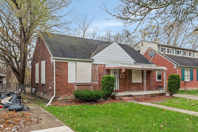 view of front facade featuring covered porch, brick siding, a front lawn, and a shingled roof