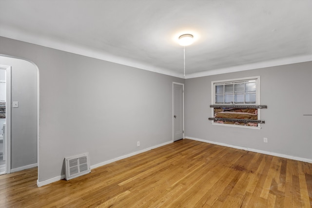 empty room featuring light wood-type flooring, baseboards, visible vents, and arched walkways