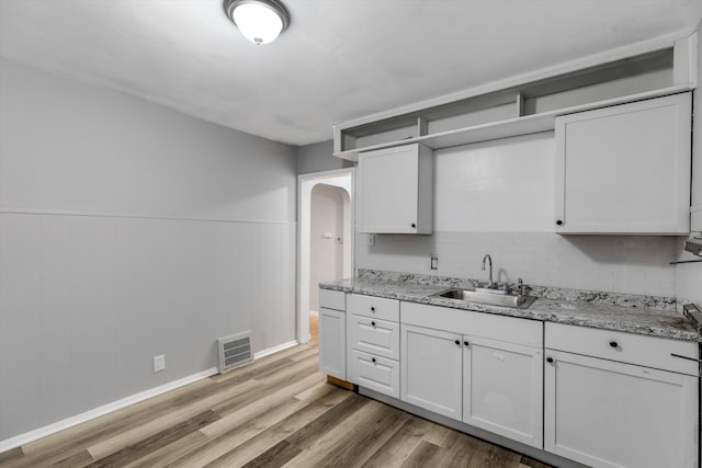 kitchen with arched walkways, light wood finished floors, visible vents, wainscoting, and a sink