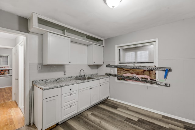 kitchen with wood finished floors, a sink, light stone counters, and white cabinets