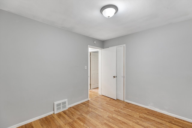 empty room with light wood-style floors, visible vents, and baseboards