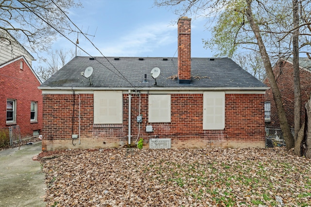 back of house with a shingled roof, a chimney, and brick siding