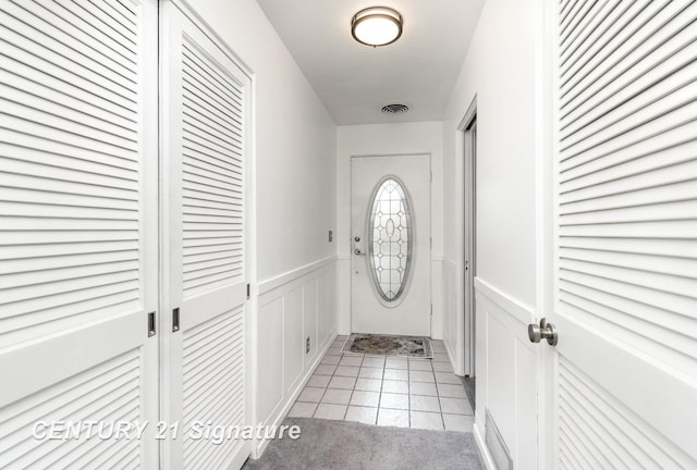 doorway with light tile patterned flooring, visible vents, and wainscoting