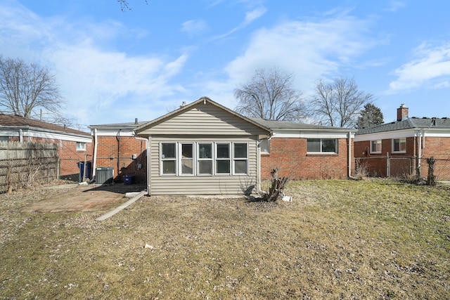 rear view of house with central air condition unit, a fenced backyard, brick siding, and a lawn