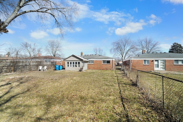 rear view of house with brick siding, a chimney, a fenced backyard, and a lawn