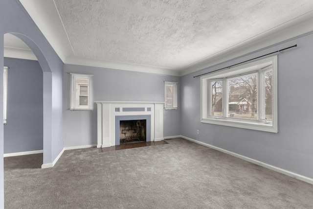 unfurnished living room featuring carpet, arched walkways, a fireplace with flush hearth, a textured ceiling, and baseboards