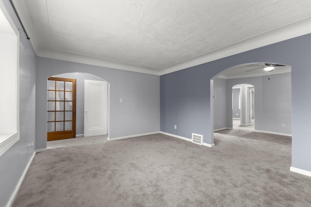 carpeted spare room featuring arched walkways, visible vents, a ceiling fan, a textured ceiling, and baseboards