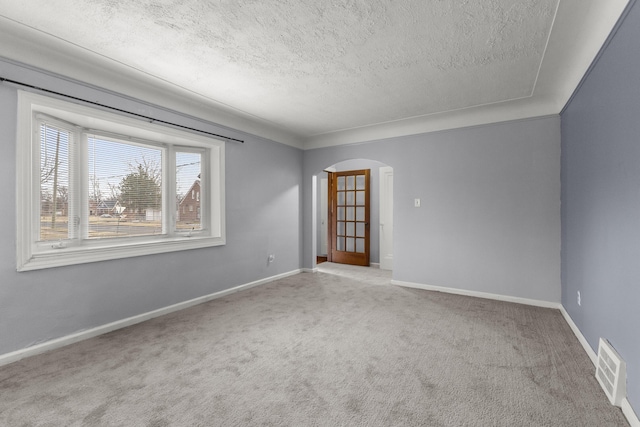 spare room featuring visible vents, arched walkways, baseboards, carpet, and a textured ceiling