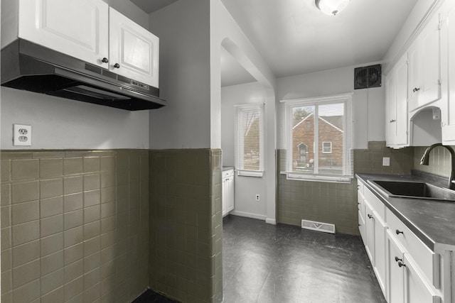 kitchen featuring visible vents, white cabinets, dark countertops, under cabinet range hood, and a sink