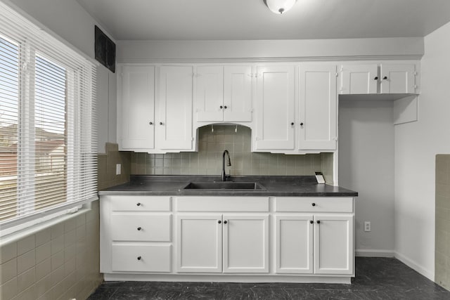 kitchen with visible vents, white cabinets, dark countertops, a sink, and backsplash