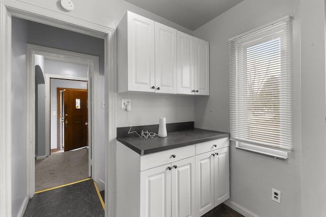 kitchen featuring a wealth of natural light, dark countertops, white cabinets, and arched walkways