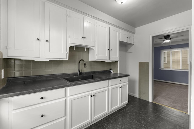 kitchen featuring dark countertops, white cabinetry, decorative backsplash, and a sink