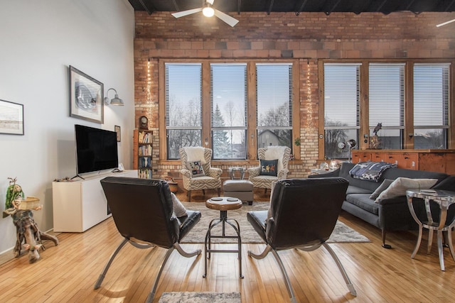 living area with light wood finished floors, brick wall, and a ceiling fan