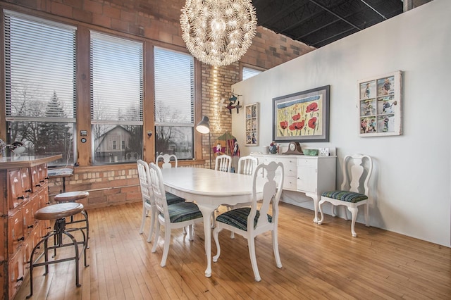 dining space featuring light wood-type flooring, brick wall, and a notable chandelier