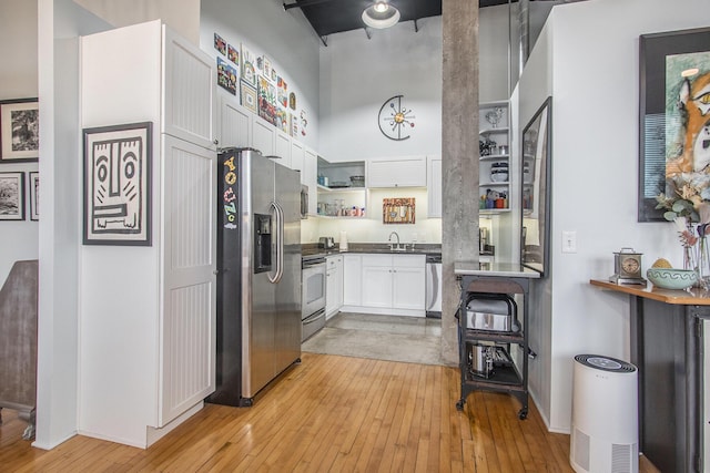 kitchen featuring open shelves, appliances with stainless steel finishes, light wood-style flooring, and a towering ceiling