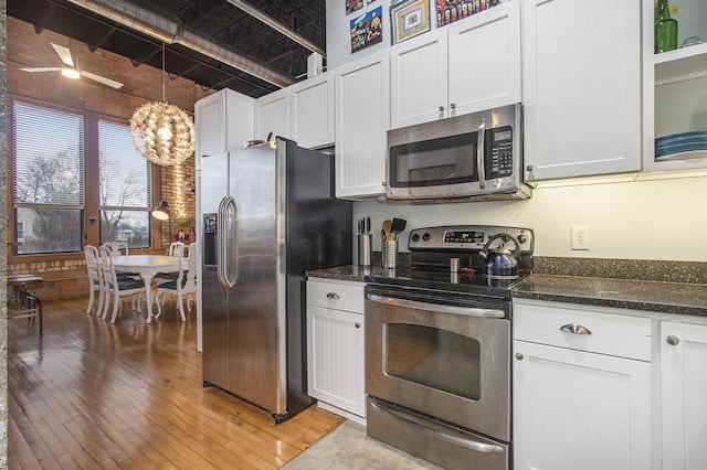 kitchen with stainless steel appliances, dark stone counters, white cabinetry, and light wood-style floors