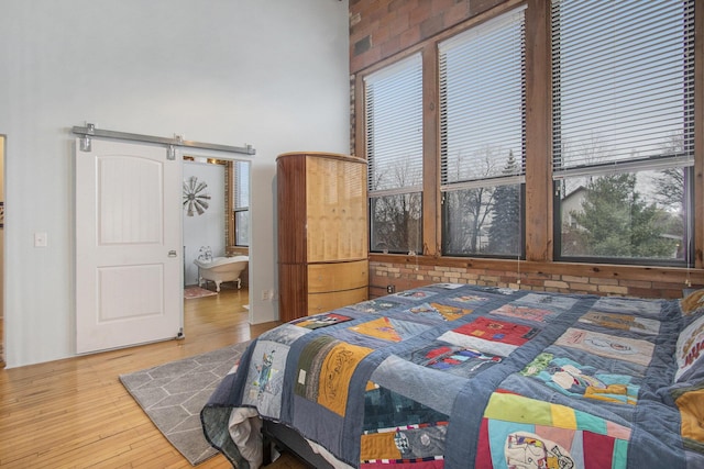 bedroom featuring wood finished floors, ensuite bath, and a barn door