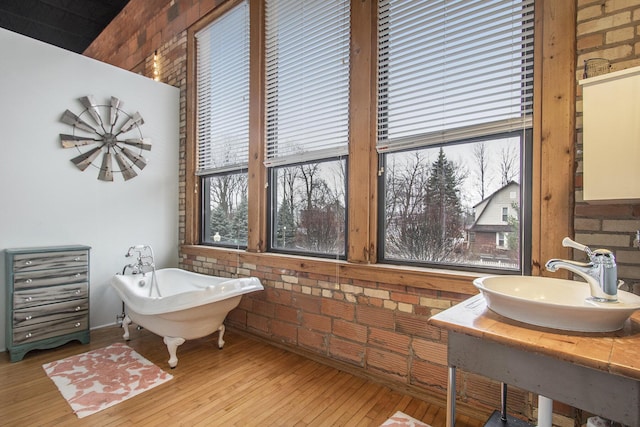 full bath featuring brick wall, a freestanding bath, wood-type flooring, and a sink