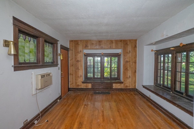 empty room with a wealth of natural light, a wall mounted AC, a textured ceiling, and wood finished floors