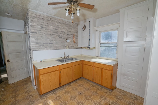 kitchen featuring light countertops, a ceiling fan, a sink, a textured ceiling, and brick wall