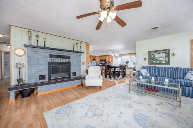 living area featuring a textured ceiling, light wood finished floors, a brick fireplace, and visible vents