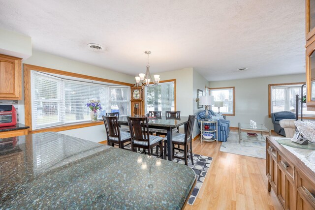 dining space featuring a notable chandelier, visible vents, a textured ceiling, light wood-type flooring, and baseboards
