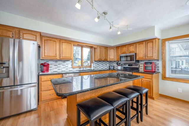 kitchen with stainless steel appliances, a sink, a kitchen breakfast bar, backsplash, and dark stone counters