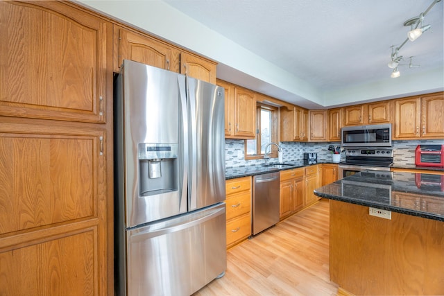 kitchen featuring brown cabinetry, dark stone counters, appliances with stainless steel finishes, light wood-style floors, and a sink